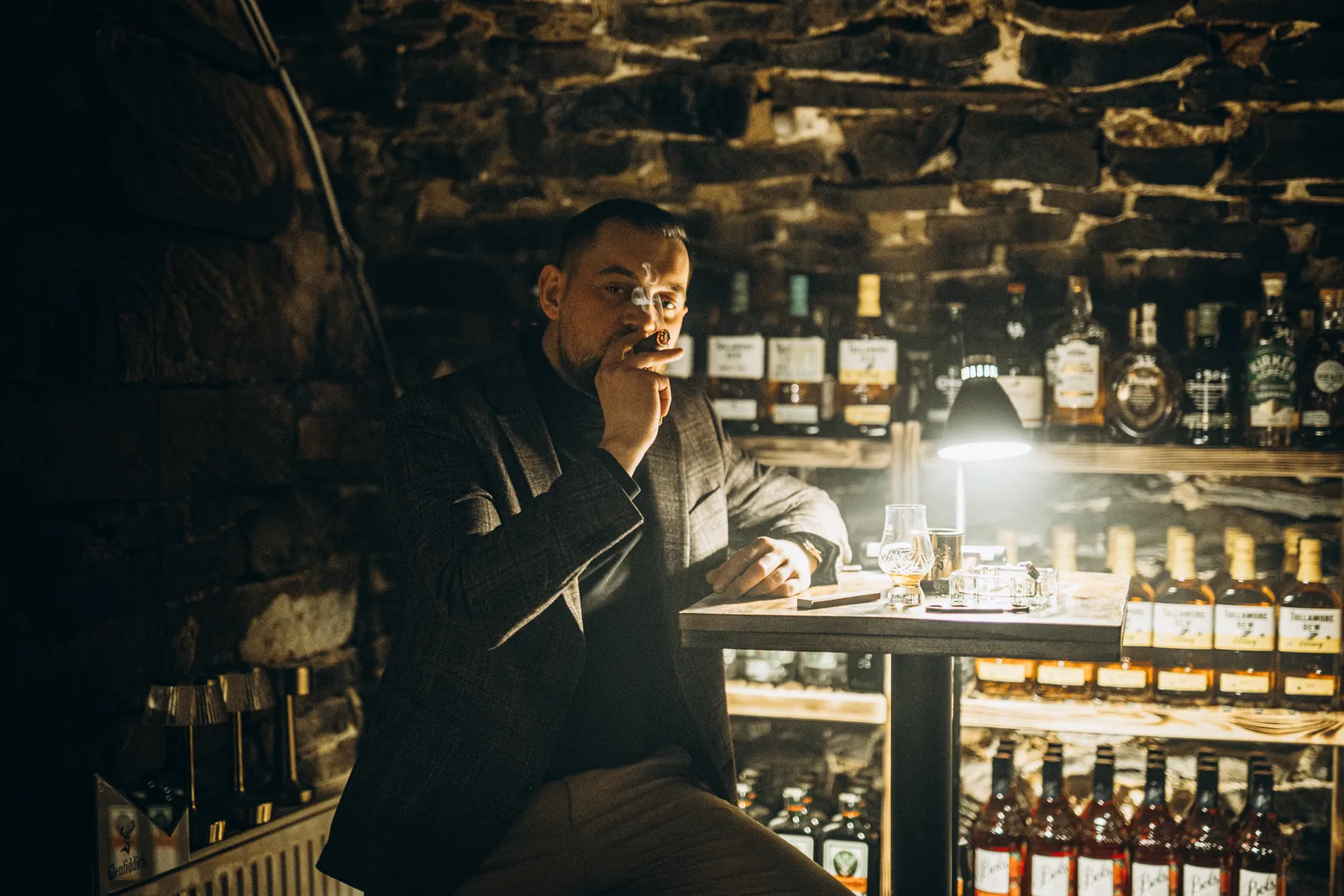 Gość przy barze na tle kamiennych ścian i półek z alkoholami