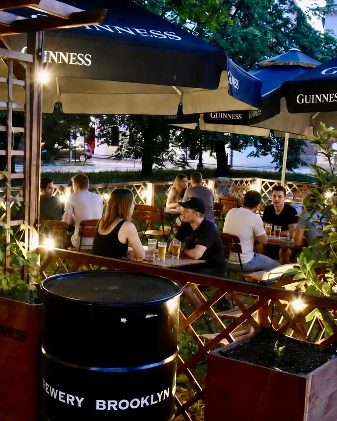 Ogródek barowy w Legnicy – Goście La Musica przy stolikach pod parasolami Guinness